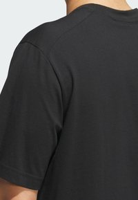 Camiseta de algodón negra con cuello redondo, mangas cortas y una textura suave. La parte de atrás presenta detalles de costura limpios.