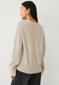 Beige gebreide sweater met een ronde hals, lange mouwen en ribgebreide manchetten. Zachte textuur, comfortabele pasvorm en zijsplitten aan de zoom.