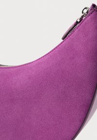 Fialová semišová topánka s oblým dizajnom, zdobená strieborným zipsom a hladkým okrajom. Textúra pôsobí mäkko a zamatovo.