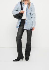 Žena oblečená v světle modré džískové bundě, bílé košili, černých kožených kalhotách, černých kožených lodičkách kitten heels a nese černou kabelku přes rameno.