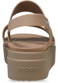 Bruine platform sandalen met brede gekruiste banden, gemaakt van een glad synthetisch materiaal, met een gestructureerde voetbed en het merkembleem op de zool.