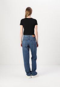 T-shirt noir à manches courtes associé à un jean en denim bleu taille haute, avec une pièce en cuir à la taille et une coupe ample.