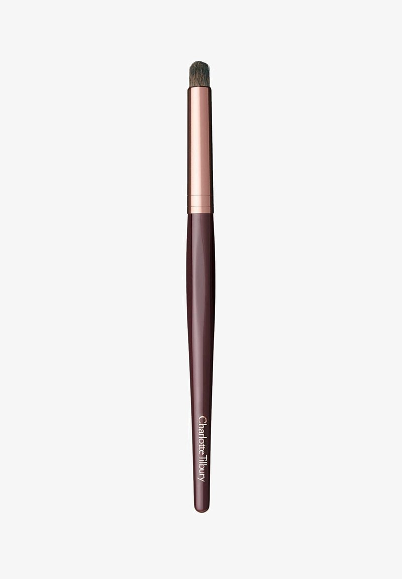 Pennello per trucco con un manico di un intenso bordeaux scuro, ghiera in oro rosa e setole dense e arrotondate. Presenta il marchio "Charlotte Tilbury" sul manico.
