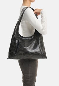 Borsa a tracolla in pelle nera con una texture liscia e lucida, forma grande e arrotondata e una tasca laterale con zip.