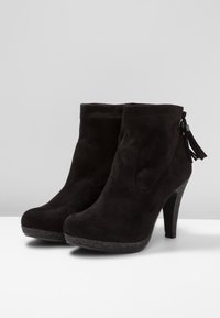 Bottines en suède noir avec un talon haut, un bout arrondi, des découpes sur les côtés et un accent en frange sur la fermeture éclair. Semelle extérieure texturée.