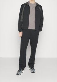 Svart hoodie med grå detaljer, tillsammans med matchande svarta sweatpants. Grå t-shirt under. Bekväma sneakers med ett texturerat mönster.