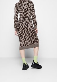 Abito a maglia con motivo geometrico marrone e beige, silhouette aderente, polsini e orlo a costine, abbinato a scarpe nere chunky e calzini verde neon.