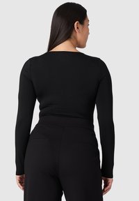 Musta pitkähihainen paita, joka on istuva vyötäröltä ja jossa on leveä kaula-aukko. Sileä kangas, jossa on minimaalinen saumat, yhdistettynä mustiin korkeavyötäröisiin housuihin.