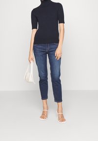 Námořnický rolák, krátké rukávy, v kombinaci s úzkými tmavými džíny a průhlednými podpatky. Drží světle béžovou kabelku.