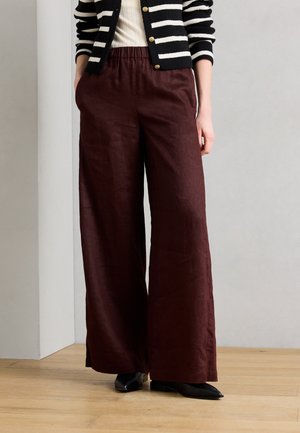 Naine kannab kõrge vöökohaga, laia säärega tumepruune pükse, musti teravaid kingi, valget soonikutatud topi ja must-valget triibulist kardigani kuldsete nööpidega.