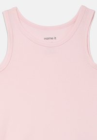 Jasnoróżowy bawełniany top na ramiączkach z okrągłym dekoltem, szerokimi ramiączkami i gładką fakturą. Posiada metkę z nazwą marki "name it".