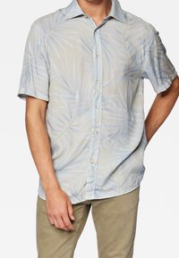 Camisa de manga corta con botones en color beige claro con estampado de hojas de palma azules; tela suave, cuello estándar y corte holgado.