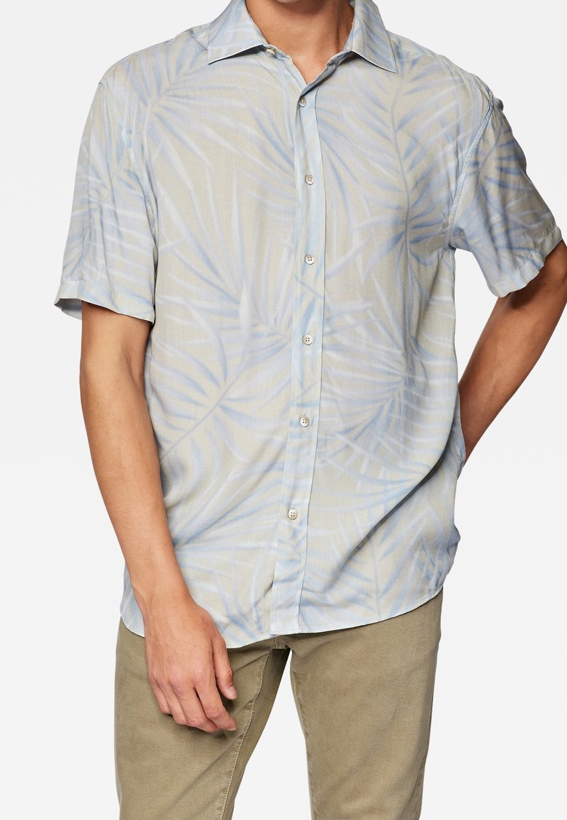 Camisa de manga corta con botones en color beige claro con estampado de hojas de palma azules; tela suave, cuello estándar y corte holgado.