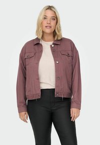 Roza denim jakna z gumbi na sprednji strani, dvema žepoma na prsih in skrajšano prileganjem. Nošena nad svetlo puloverjem in črnimi hlačami.
