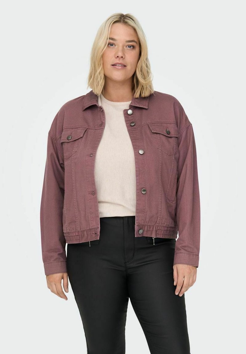 Roza denim jakna z gumbi na sprednji strani, dvema žepoma na prsih in skrajšano prileganjem. Nošena nad svetlo puloverjem in črnimi hlačami.