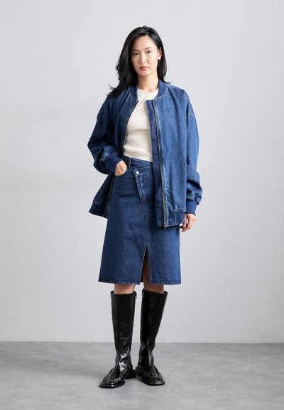 Denim švarkas su suspaustomis rankovėmis, prigludusi džinsinė sijonas su priekine plyšiu, ir juodi blizgūs batai iki kelių. Po švarku neitrali viršutinė dalis.