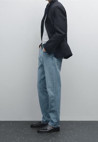 Black blazer, white shirt, and light blue loose-fitting jeans. Black slip-on shoes. Minimalist design, smooth texture, and neutral colors.