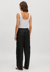 Zwarte cargo broek met twee zijzakken, elastische tailleband en losse pasvorm, in combinatie met een witte tanktop, gezien van achteren.
