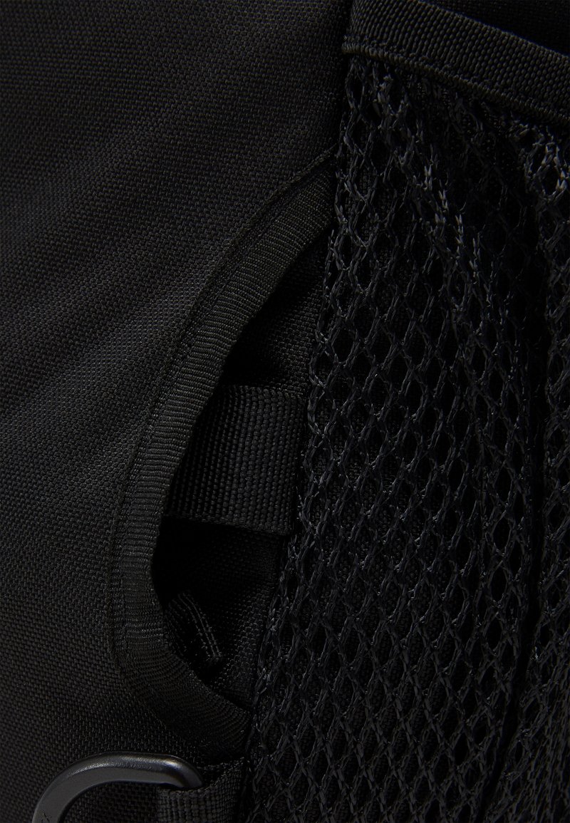 Gros plan d'une poche d'un sac à dos en tissu noir avec un panneau latéral en mesh et une boucle de sangle noire à l'intérieur de la poche.