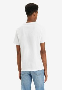 Camiseta de algodón blanca con cuello redondo y mangas cortas, combinada con jeans de mezclilla azul claro. Diseño simple y clásico sin patrones notables.