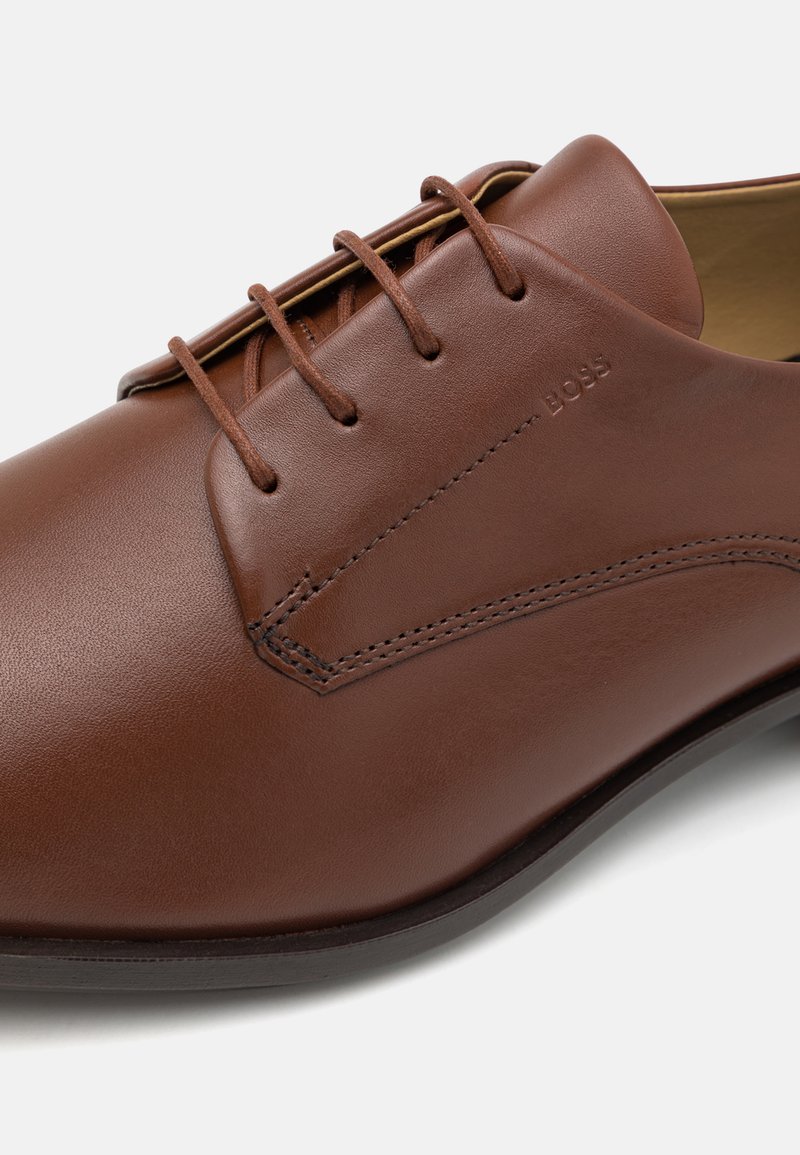 Brown leather dress shoe with a smooth finish, featuring a rounded toe, five eyelets for laces, and subtle stitching detail.