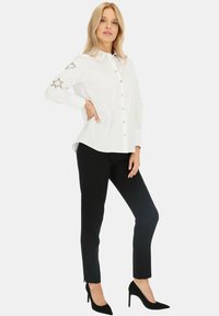 Biała koszula z kołnierzykiem typu point, ozdobiona srebrnymi gwiazdkami i serduszkami na rękawach, zestawiona z czarnymi dopasowanymi spodniami.