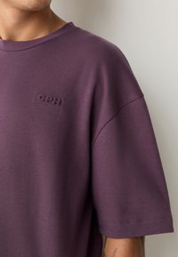 Lila kurzärmliges T-Shirt aus weichem Stoff, mit dezentem GPH-Logo auf der Brust. Lockere Passform mit glatter Textur und sauberer Naht.