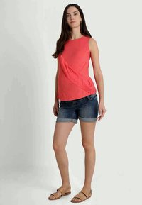 Top sem mangas de cor de coral com drapeado assimétrico, combinado com calções de ganga escuros com bainhas dobradas. Usado com sandálias rasas.