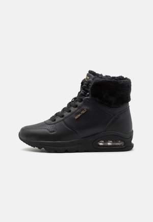 Svart højhælede sneakers med en polstret faux fur krave, tekstureret læder, perforerede detaljer og en synlig luftenhed i sålen.