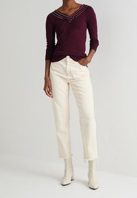 Burgundy long-sleeve top with studded neckline, paired with off-white, cropped jeans and white ankle boots with a slight heel.