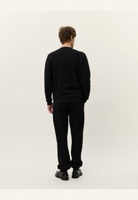 Sweatshirt negru și pantaloni joggeri asortați dintr-un material moale. Puloverul are guler rotund și manșete ribbate; pantalonii joggeri au o talie elastică și manșete.