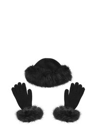 Conjunto de gorro de punto negro y guantes, cada uno con un borde de pelaje negro suave, dispuestos por separado sobre un fondo blanco.