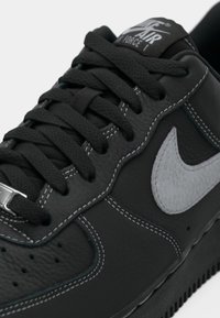 Black leather sneaker with gray accents, featuring a textured surface, prominent laces, and white stitching. Nike logo displayed on tongue.