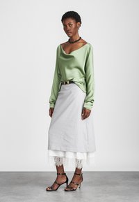 Πράσινη σατέν μπλούζα με μακριά μανίκια συνδυασμένη με μια ανοιχτή γκρι φούστα με δαντελένια άκρη, συμπληρωμένη με μαύρες λεπτές γόβες και μια μαύρη ζώνη.