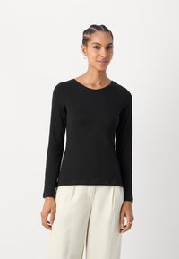 Langermet svart topp med rund hals, laget av mykt materiale. Har en tettsittende design og glatt tekstur, sammen med lyse bukser.