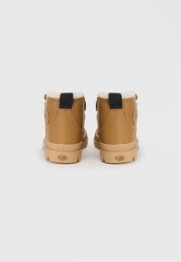 Botas de tobillo de cuero marrón con un forro interior de peluche, tirador negro y suela de goma con un patrón texturizado.