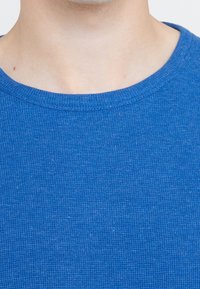 Blå kortärmad t-shirt gjord av textilerat tyg med rundad halsringning. Materialet verkar mjukt och något ribbat.