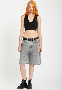 Un crop top noir à côtes associé à un bermuda en denim gris avec une ceinture noire. Le modèle porte des bottes noires à lacets.