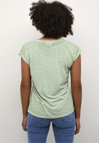 T-shirt verde a maniche corte con orlo arrotondato, realizzato in un tessuto texturizzato. La vista posteriore mostra leggere variazioni di colore e forma.