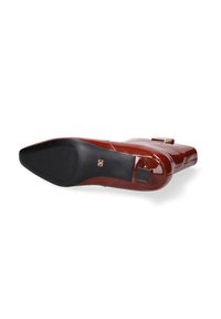Rode gepatineerde leren schoen met een spitse neus, een gladde textuur, een lage hak en een gouden accent aan de zijkant. Zwarte rubberen zool voor grip.