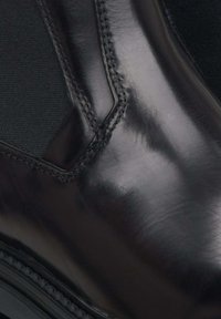 Czarne skórzane botki za kostkę o gładkim wykończeniu, z elastycznymi panelami bocznymi i widocznymi detalami szwów. Okrągły nos i solidna gumowa podeszwa.