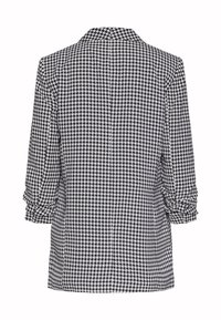 Chaqueta de mujer en un patrón de pata de gallo en blanco y negro, con cuello estructurado, mangas de tres cuartos con puños enrollados y textura de tela suave.