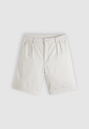 Svetlo bež kratke hlače dolžine do kolen z sprednjimi naborki, stranskimi žepi, zankami za pas in zgornjim gumbom na svetlo sivi podlagi.