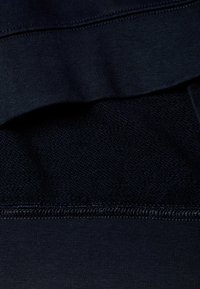 Námořnická látka s hladkým, elastickým povrchem, viditelným šitím a texturovanou panely dole. Čisté hrany a rovnoměrné švy jsou patrné.