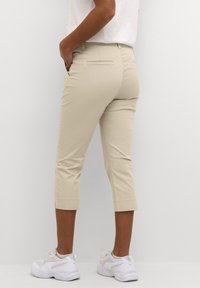 Beige cropped pants with back pockets, smooth texture, and a fitted design. Worn with white sneakers, showing a casual style.