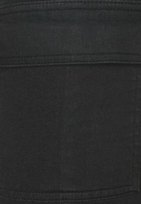 Černá látka s hladkým povrchem. Obsahuje detaily prošití a design kapsy na nášivku. Materiál se zdá být elastický a přiléhavý.
