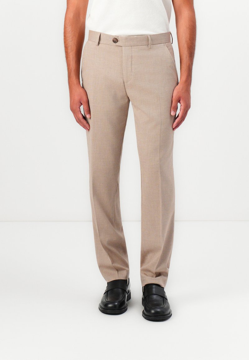 Beige szövetnadrág, texturált felülettel, egyenesen szabott fazonnal és egy gombos záródással, fekete slip-on cipővel párosítva.