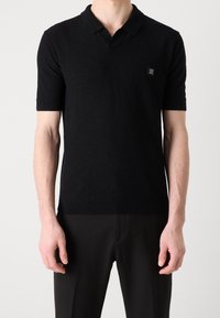 Zwarte polo met korte mouwen van een gebreide stof, met een klassieke kraag, voorzien van een klein vierkant logo op de linkerkant van de borst en ribbelboorden.