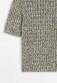 Pull en maille à manches courtes avec un fil épais et texturé en blanc et vert foncé sur un fond uni.