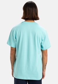 Camiseta de algodón azul claro con cuello redondo y mangas cortas, con un corte relajado y una textura suave en la vista trasera.